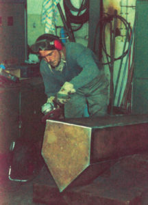 Künstler Thomas Nicolai beim bearbeiten einer Steele mit der Flex in der Werkstatt.